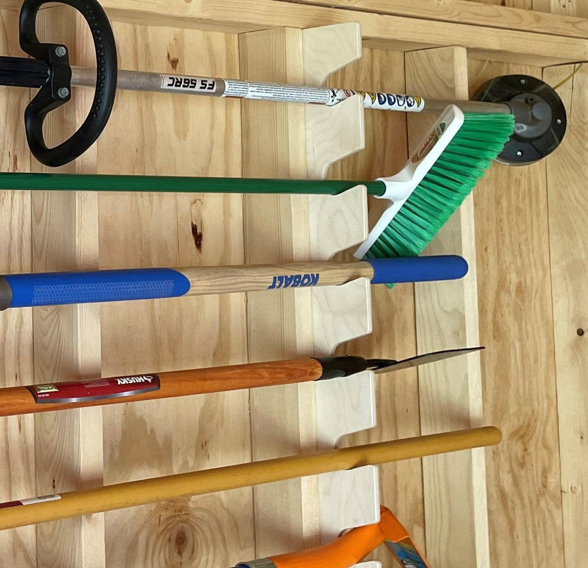 Stud-mounted garden tool organizer rack holding long-handled tools